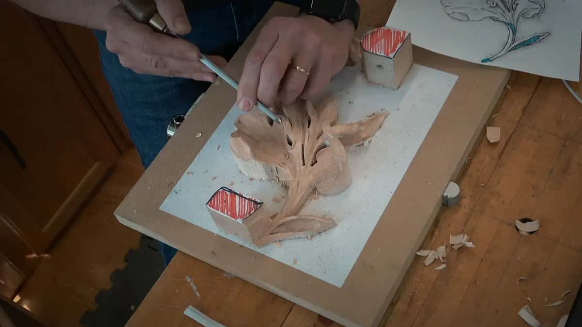 A drawing on paper beyond the board while two hands guide a slim tool into the leaf