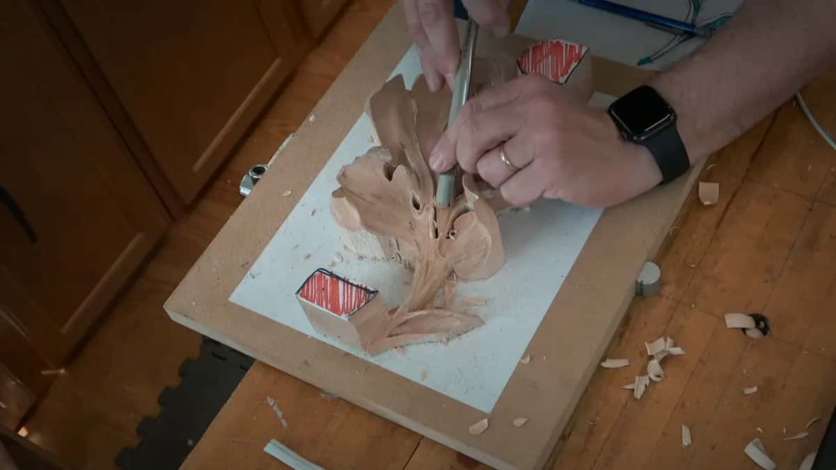 From above, a straight tool tilts down the middle lobe, a watch at the wrist and shavings on the bench