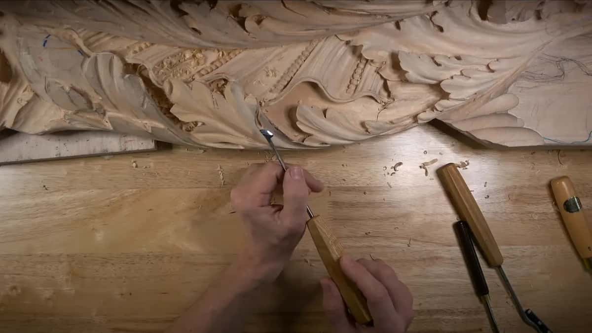 Under the frieze Both hands on a small gouge up under the frieze, three more tools on the bench