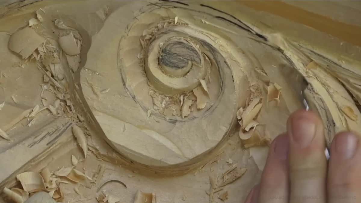 Spiral volute Spiral volute part carved, shavings everywhere, fingers holding a blade at the right of the frame