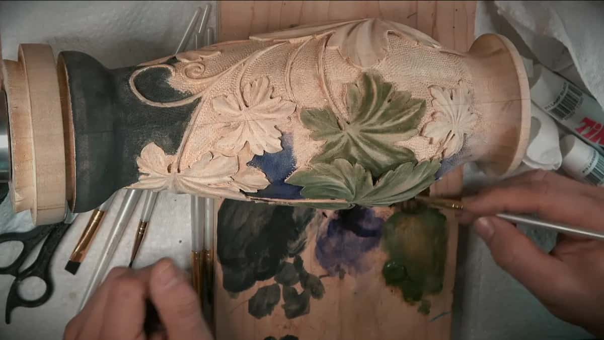 Fine brush tip running along the bottom edge of a green leaf, close to the flared rim of the vase