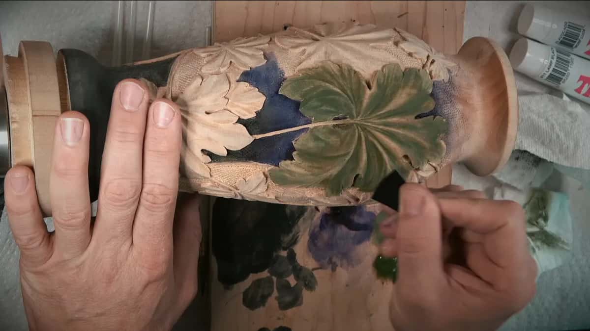 A small black scraper meets the lower edge of the leaf while the other hand holds the vase still