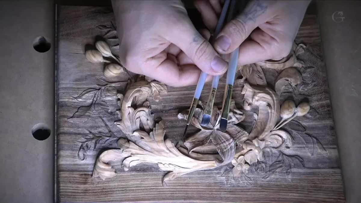 Two artist brushes over a stained box lid carved with lilies and olives.