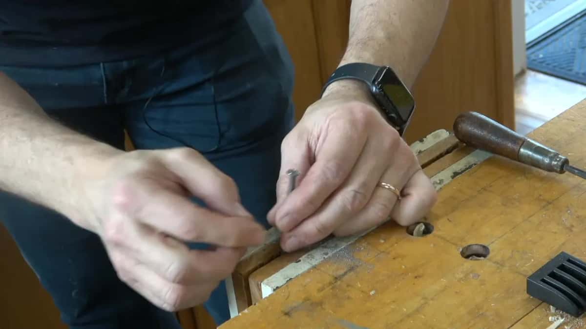 Short nail pinched between his fingers at the vise
