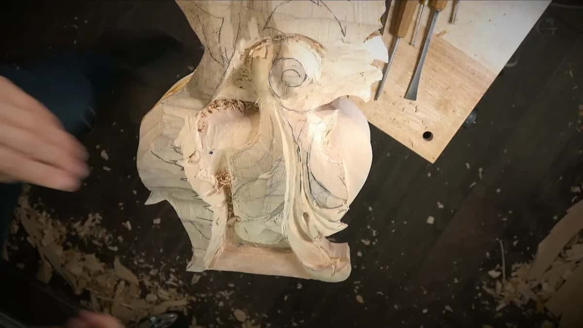 Looking down on a big carved scroll on a dark surface, gouges lying on a board beside it