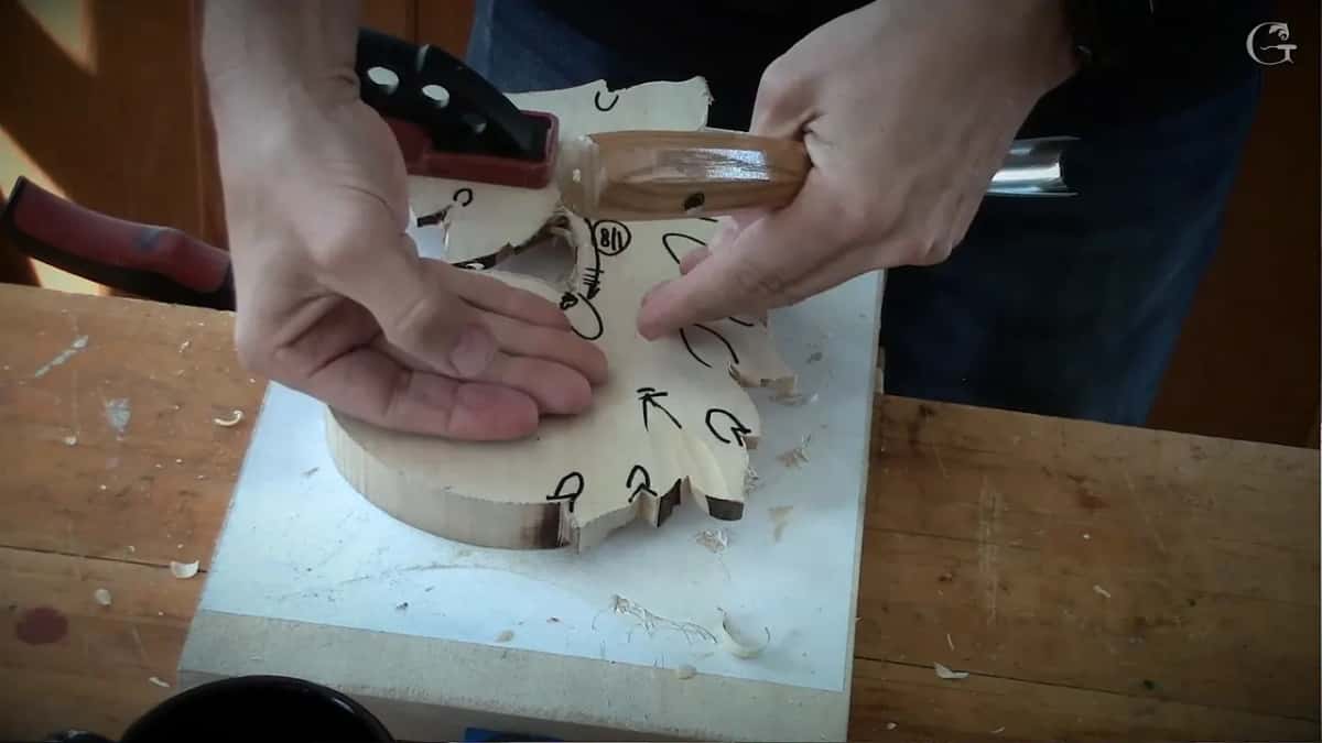 Leaf clamped upside down, its back marked with circles and arrows, one hand flat, one on a gouge