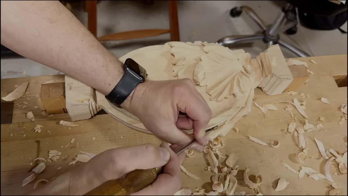Two hands carving at the leaf end of the tray while shavings pile up on the bench around it