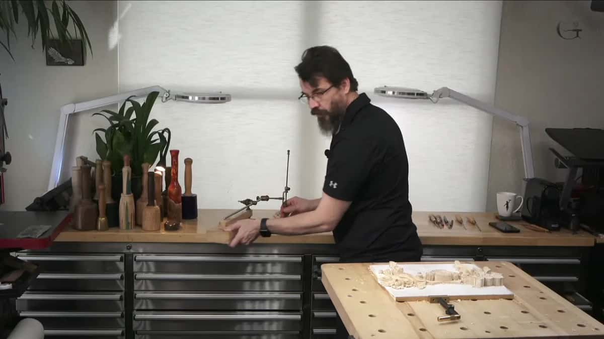 Standing at the back bench, hands on a pointing machine clamped over a carving