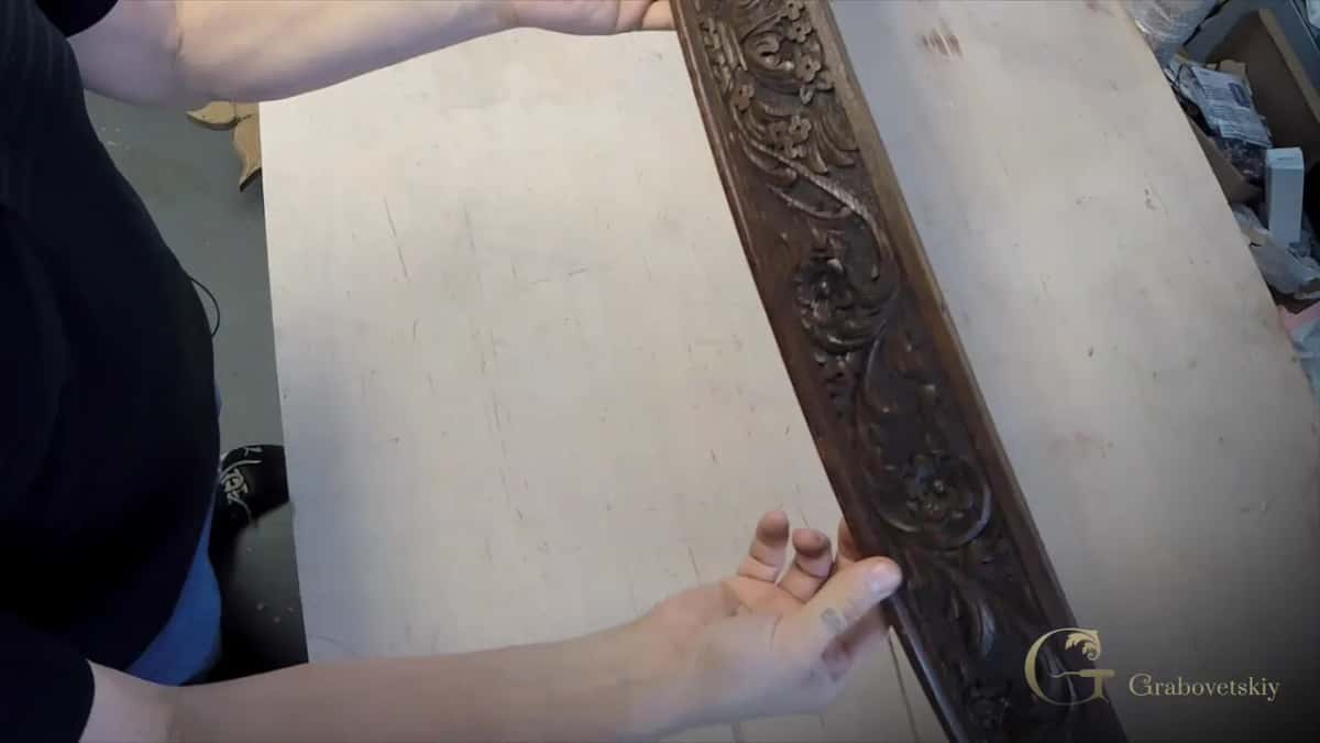 Both hands hold the old dark carved apron section