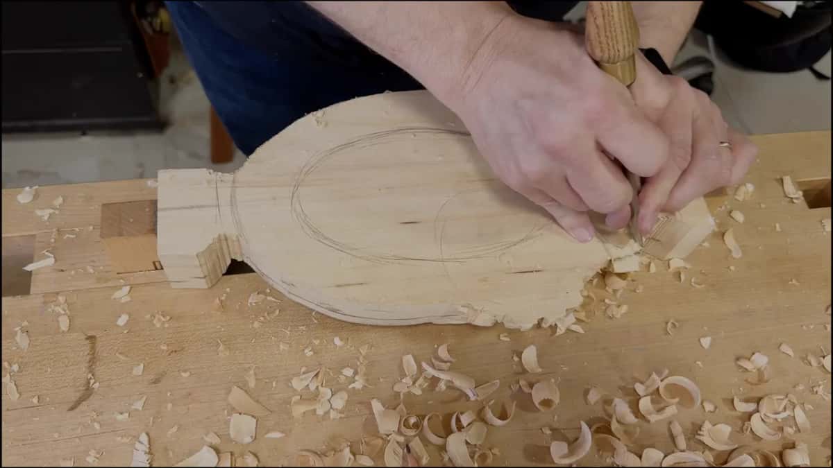 Both hands on one gouge at the thin end, fingers resting on the wood