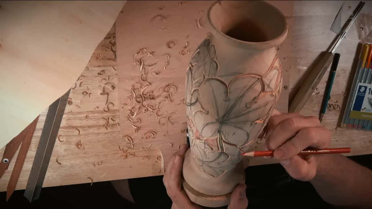 A colored pencil shading background patches between the outlined leaves, a gouge and markers lying on the bench