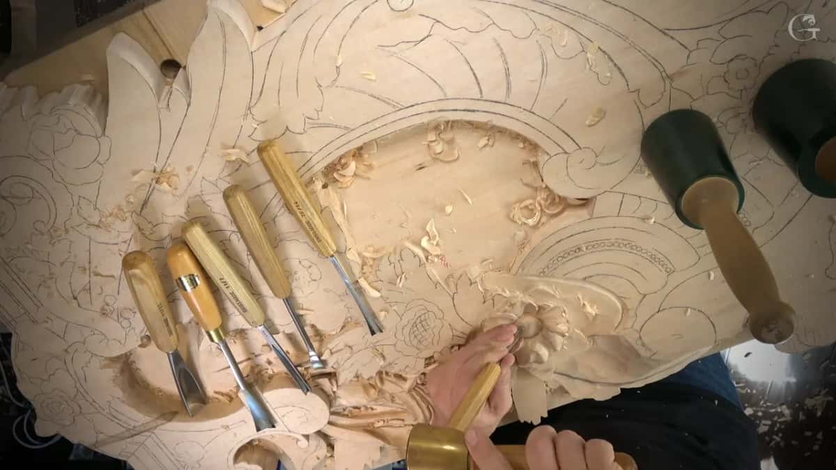 A row of gouges lies across a big drawn panel while a hand works at one small flower.
