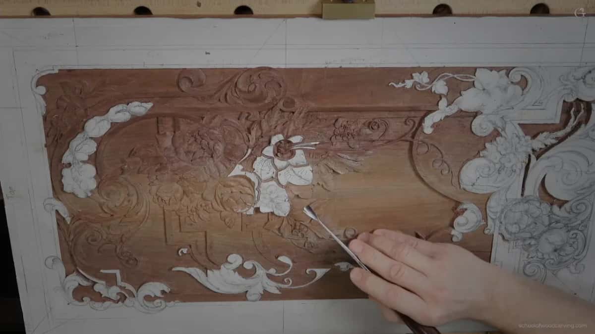 A hand holds a slim tool on a reddish carved panel with white paper shapes