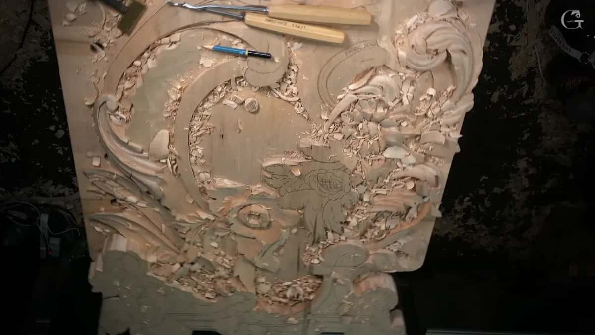 Tools and a blue pen rest across the top of a deep, half-carved panel full of leaves and scrolls