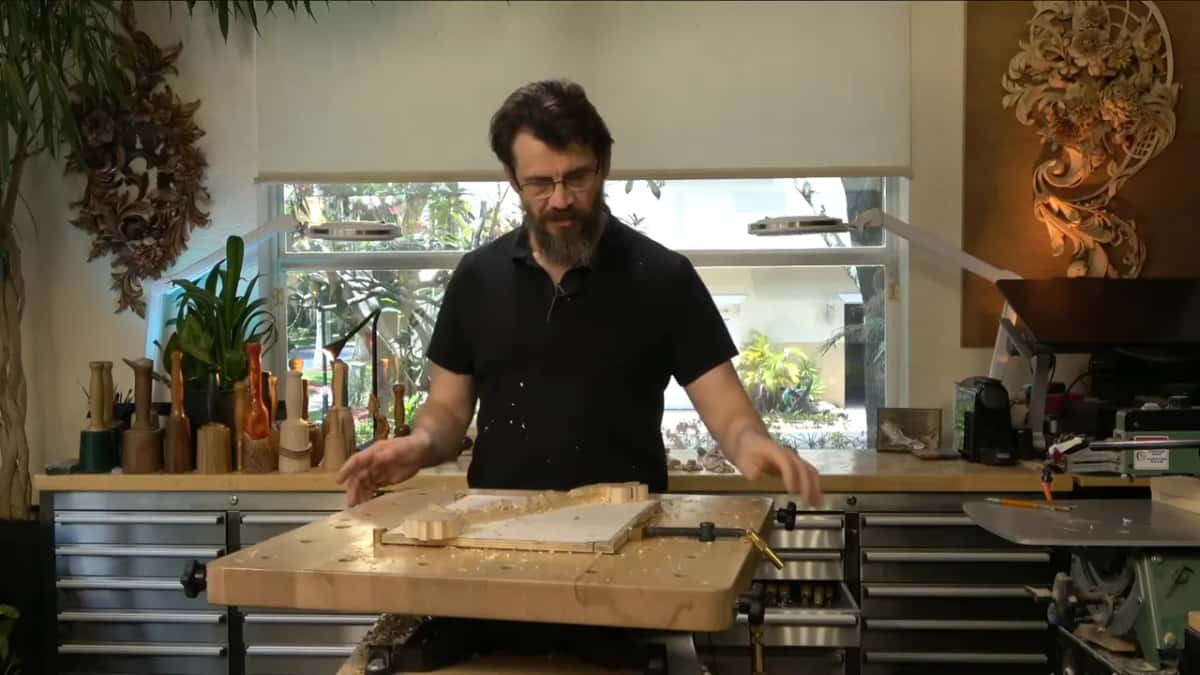 A thick bench top tipped toward the carver, a carving clamped across it and a black knob on its side