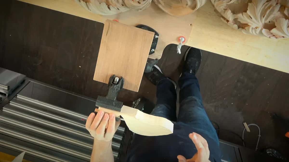 From above, his hand steadies a pale shaped piece of wood held in a small vise