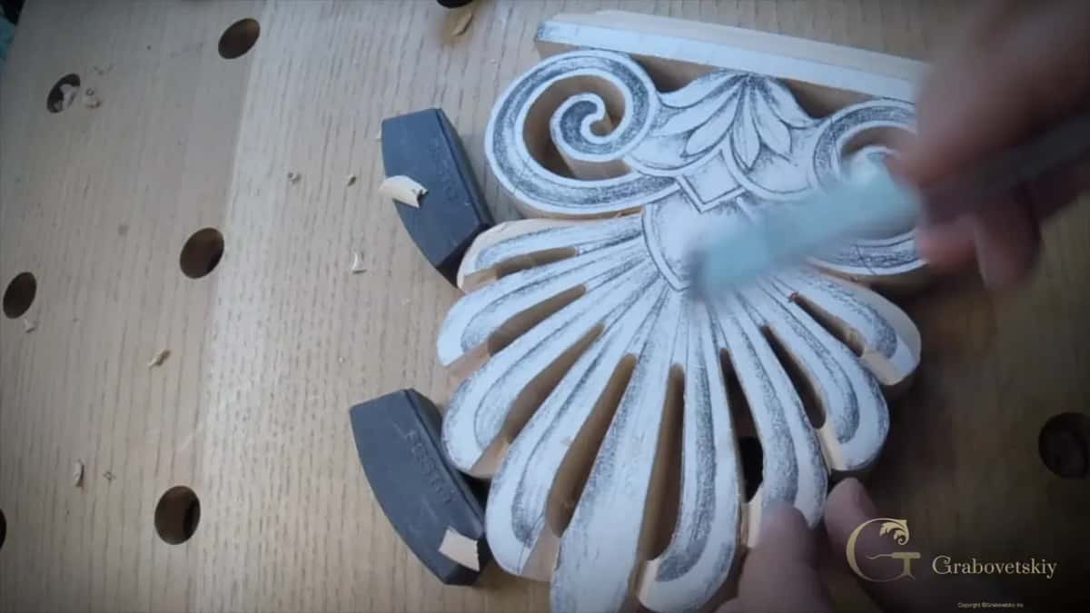 A blue handled brush sweeps chips off the scrolls, the palmette resting against two dark stops.