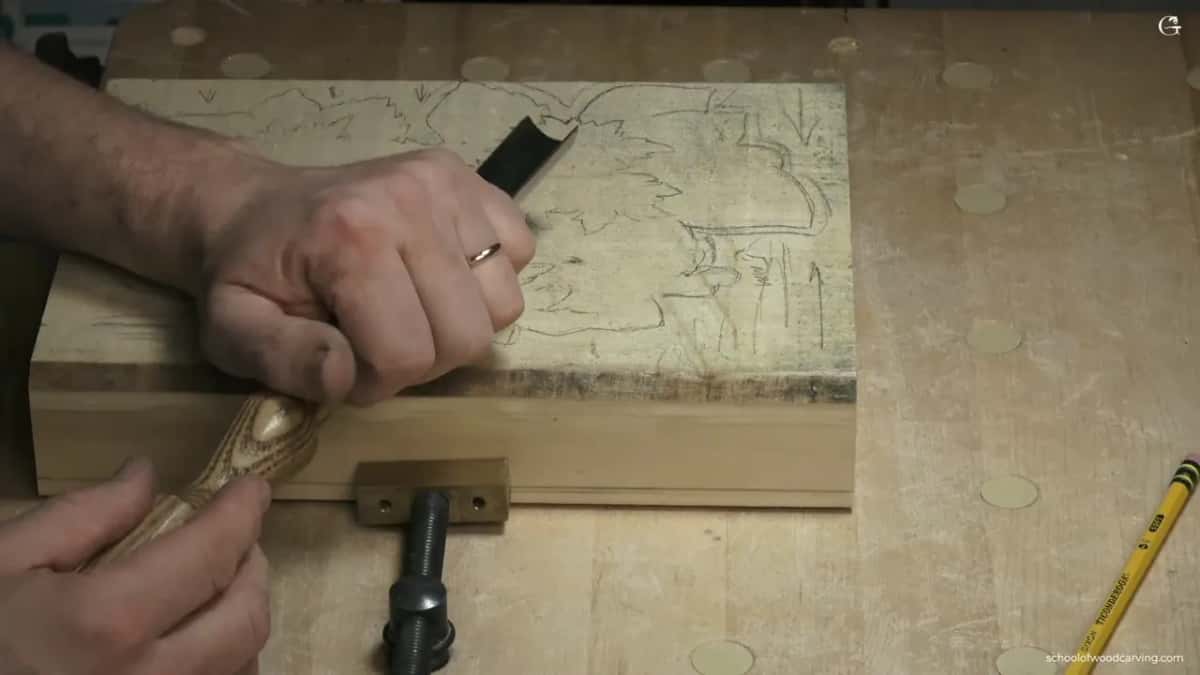 Both hands on a gouge beside the clamped block.