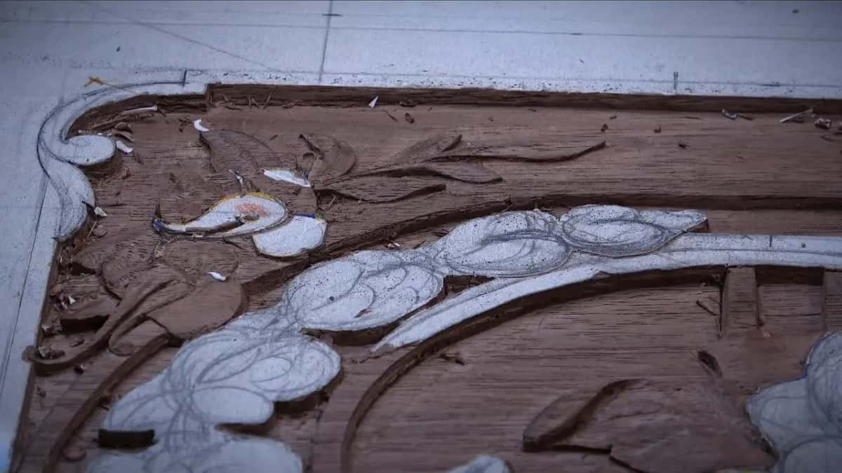 Garland of white flowers and leaves across a dark panel, a scroll curling at the corner