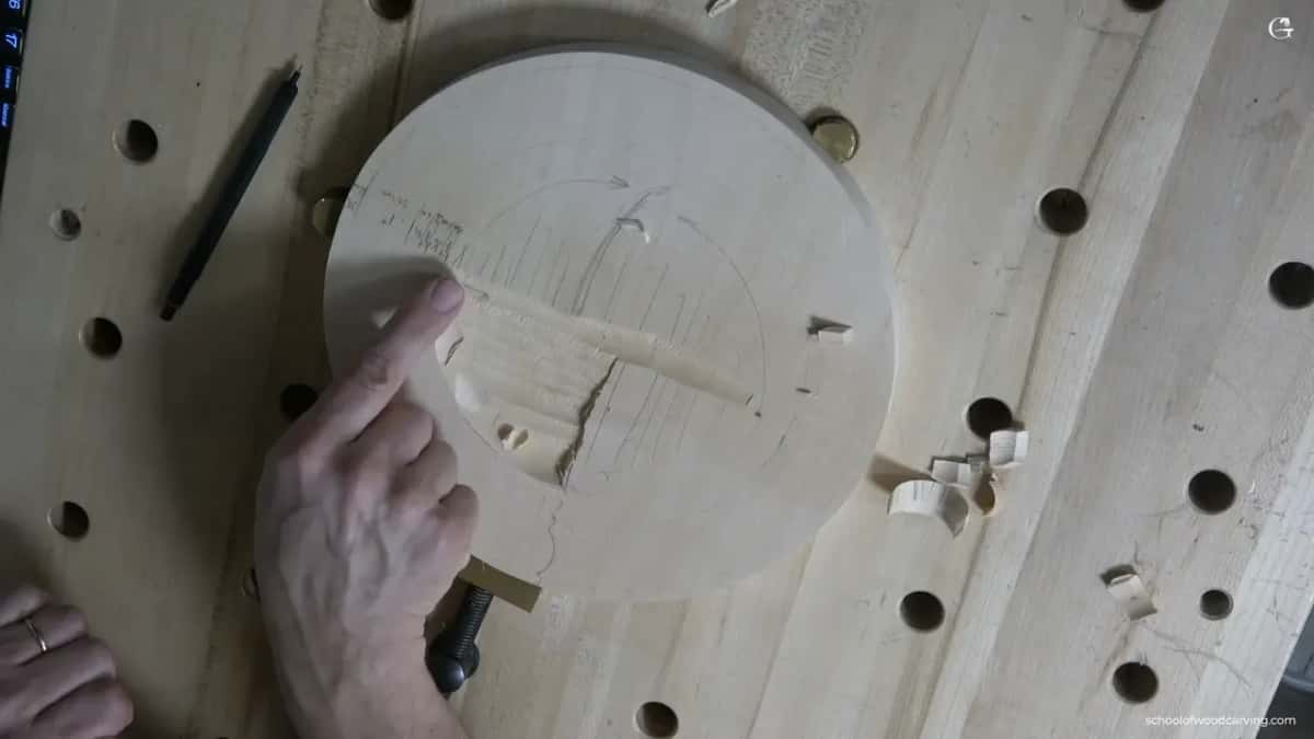 A finger beside a shallow hollow inside a pencil circle on a round blank, with a split running down through it