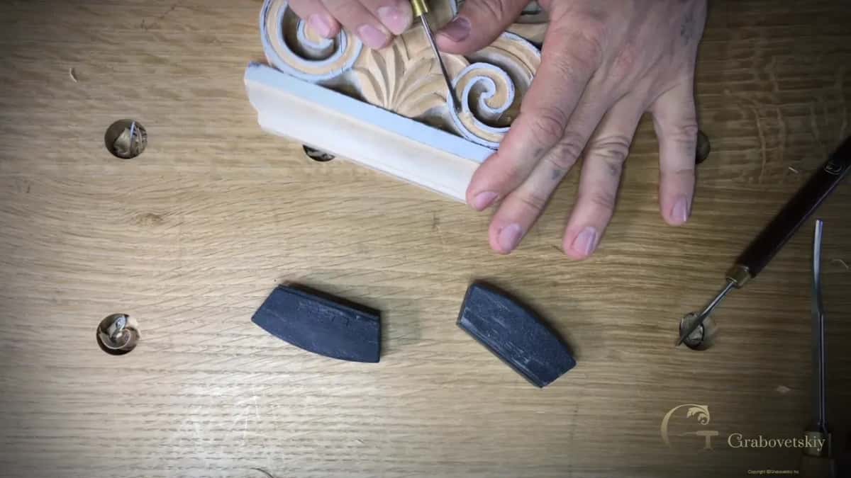 A narrow flat chisel with a brass ferrule cleans around the spiral, the free hand flat on the base