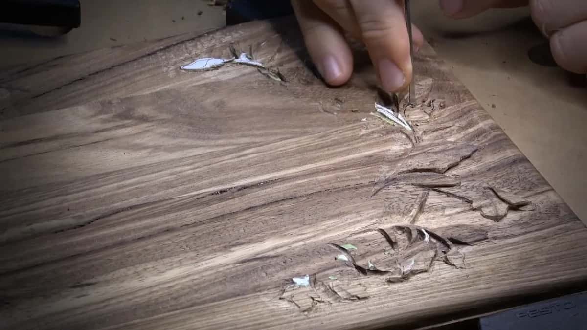 Fingertips guide a narrow tool into a tiny thorn on the dark lid