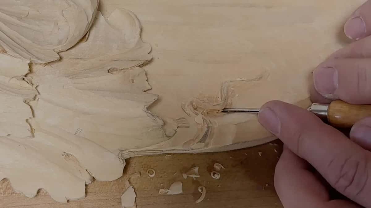 Tiny blade slipped in under the raised curl, with fresh chips lying around it on the bench