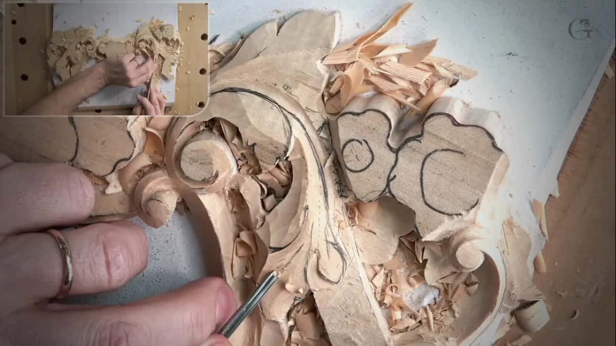 A ringed hand holds a slim tool at the edge of a carved leaf