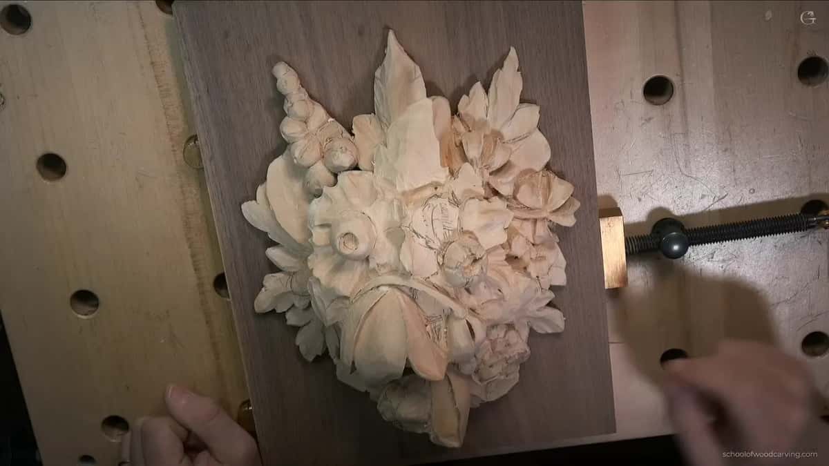 Pale carved bouquet clamped against a pegboard bench, on a dark backing board.