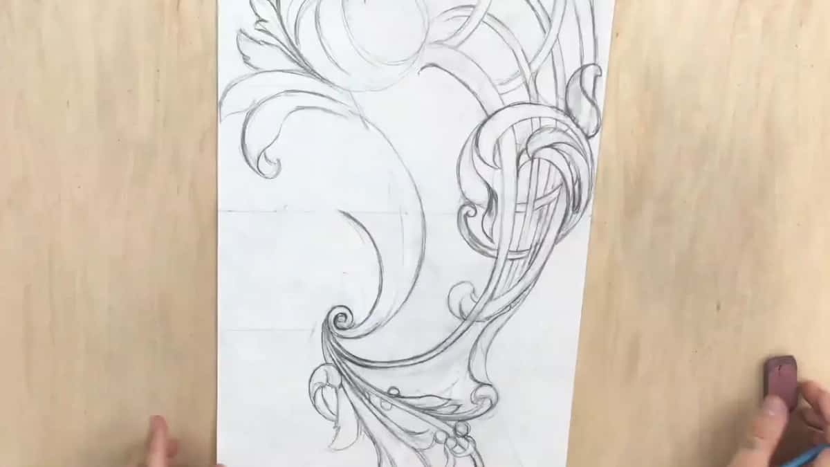 Partly drawn design turned sideways, scrolls at the bottom and a hand holding an eraser at the edge