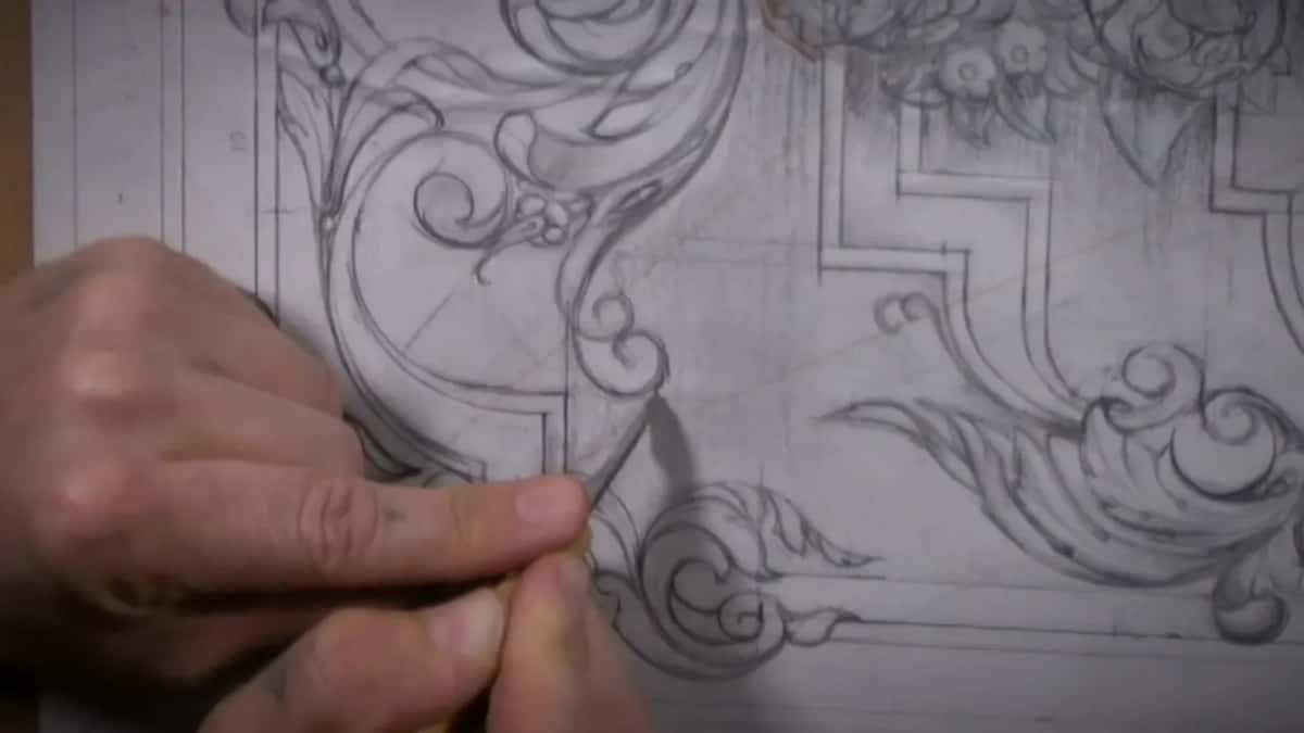 Paper drawing over the panel, fingers holding a tool at one scroll, its shadow on the paper.