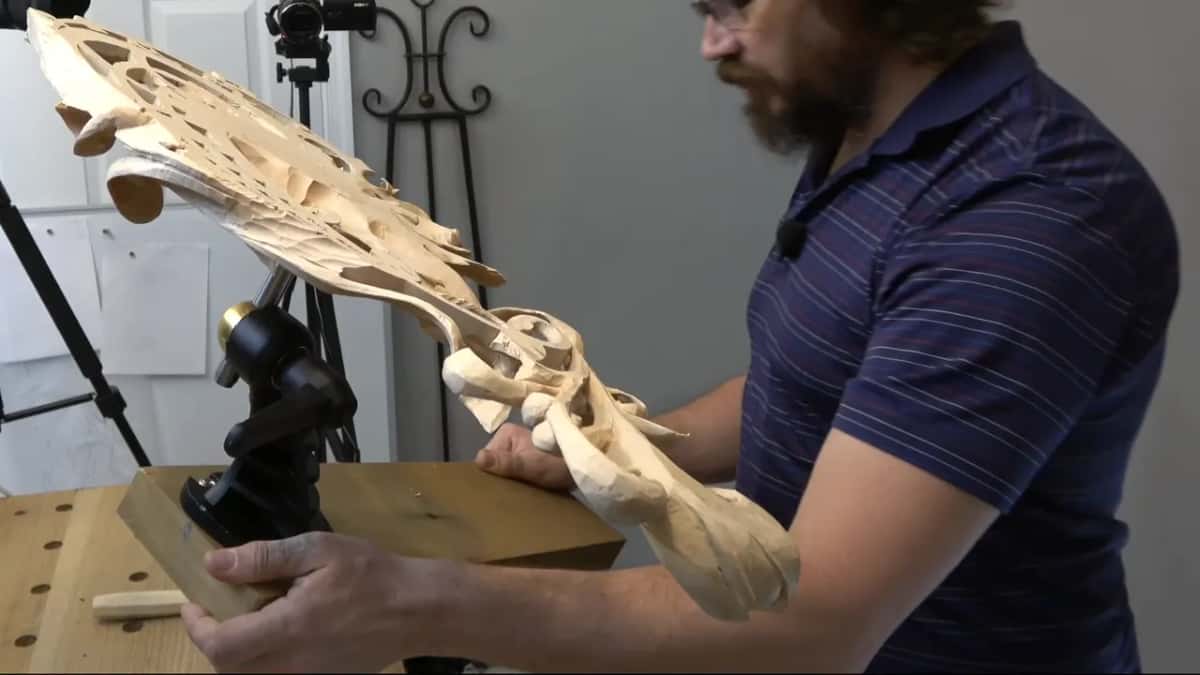 Pierced carving tipped up on a carver's vise, one hand on the block under it