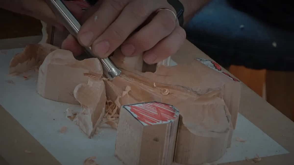 Close up, both hands on a gouge as it shapes one raised lobe beside the tab