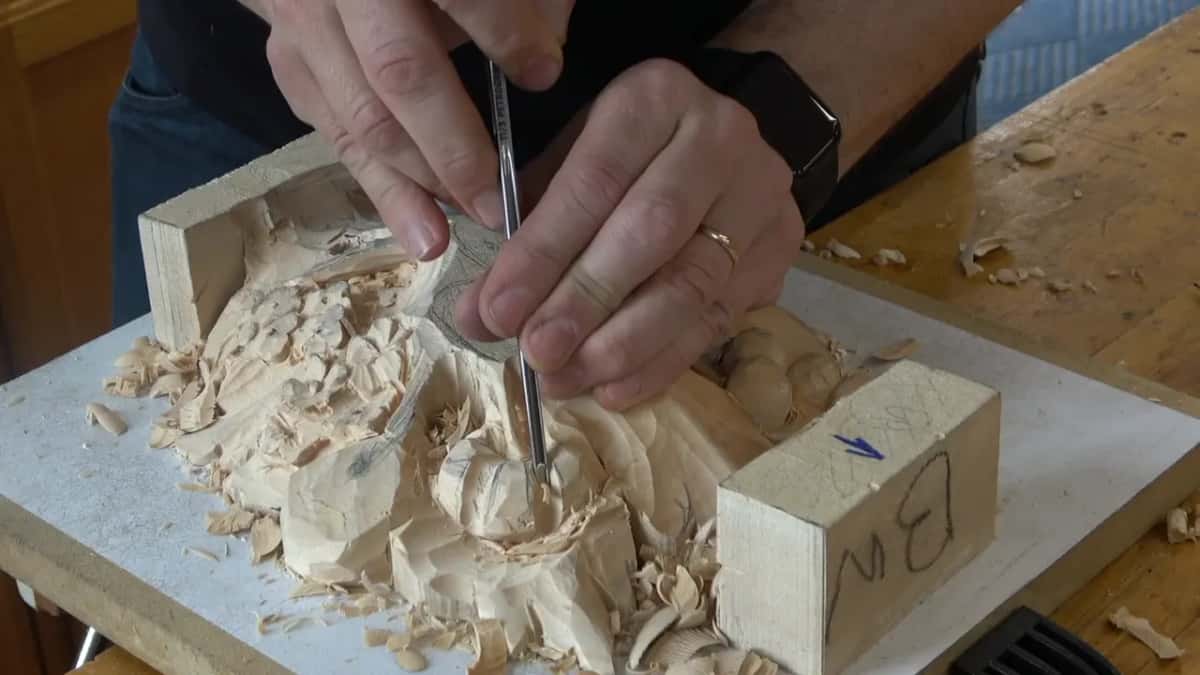 A narrow gouge pinched between two hands, point down among the loose chips
