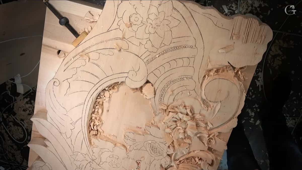 Large board covered in pencil drawing, a flower already carved near the middle and a clamp at the top corner