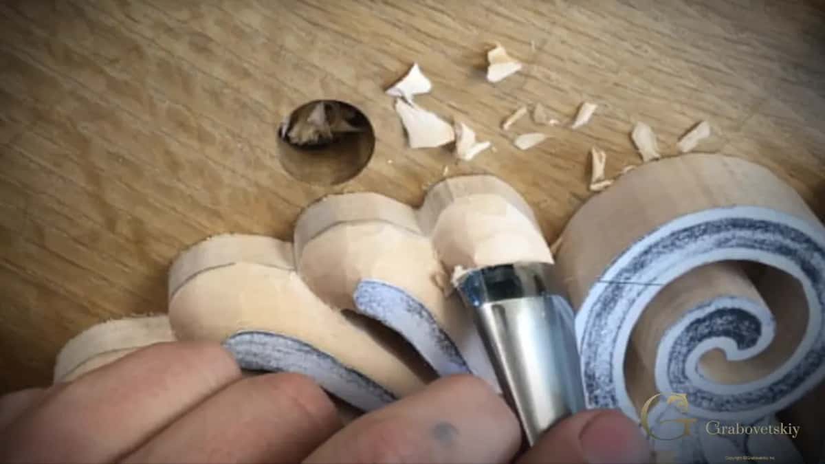 Close up, a gouge rounds over the sawn side edge next to one spiral, with pale chips lying above