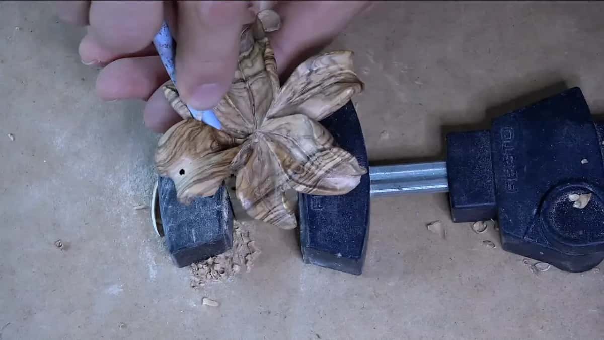 Rolled paper, tight as a tube, working one petal of the olive lily in its clamp.