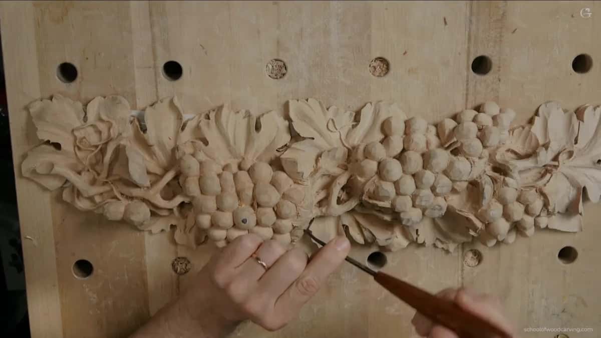 A long tool works under a carved grape garland