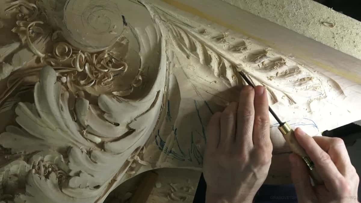 Both hands steering a slim ferruled gouge along a leaf