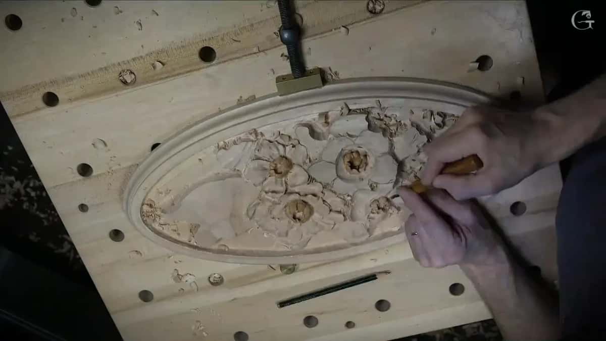 Overhead, the oval held by a metal clamp, both hands on a small tool by the flowers, a pencil below