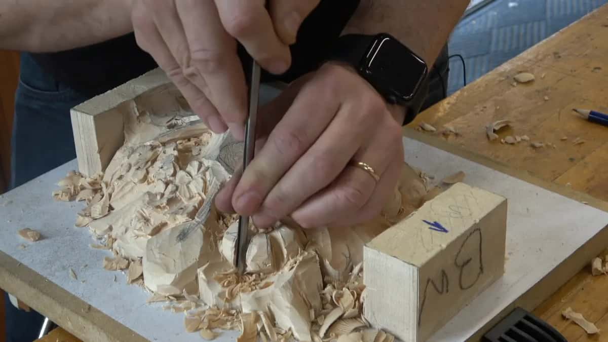 Two hands guide a slim gouge down into the lower layer, the blade leaning over to one side