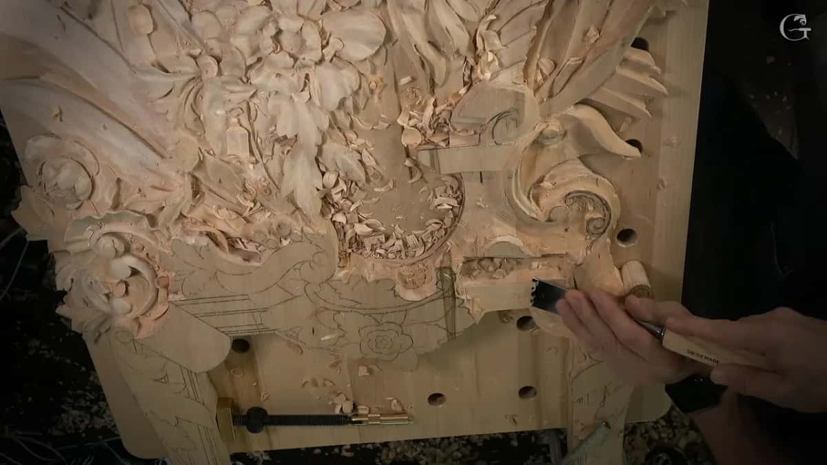 Wide gouge cleaning over the lowered section, below the carved flowers and leaves higher up