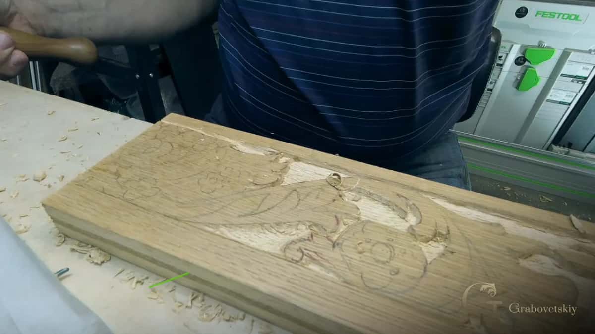 Long board with a drawn leaf, half carved, on a bench by a tool case